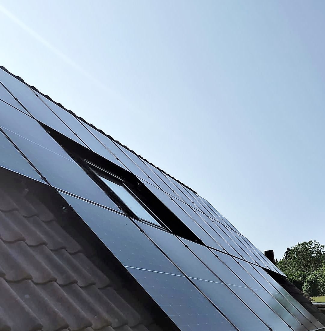 PV-Anlage auf Ziegeldach mit nahtlos integriertem Dachfenster bei blauem Himmel